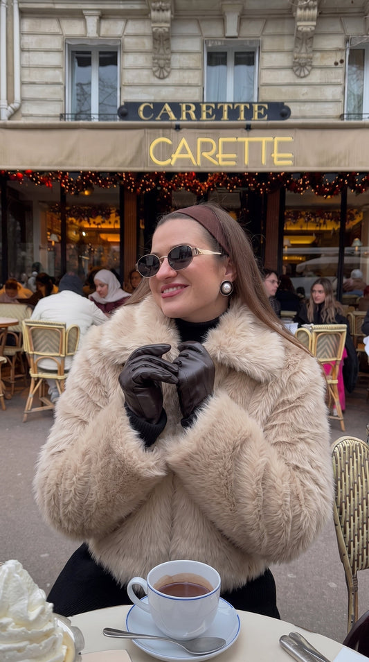 Woman wearing a beige faux fur bomber jacket with a wide collar and long sleeves