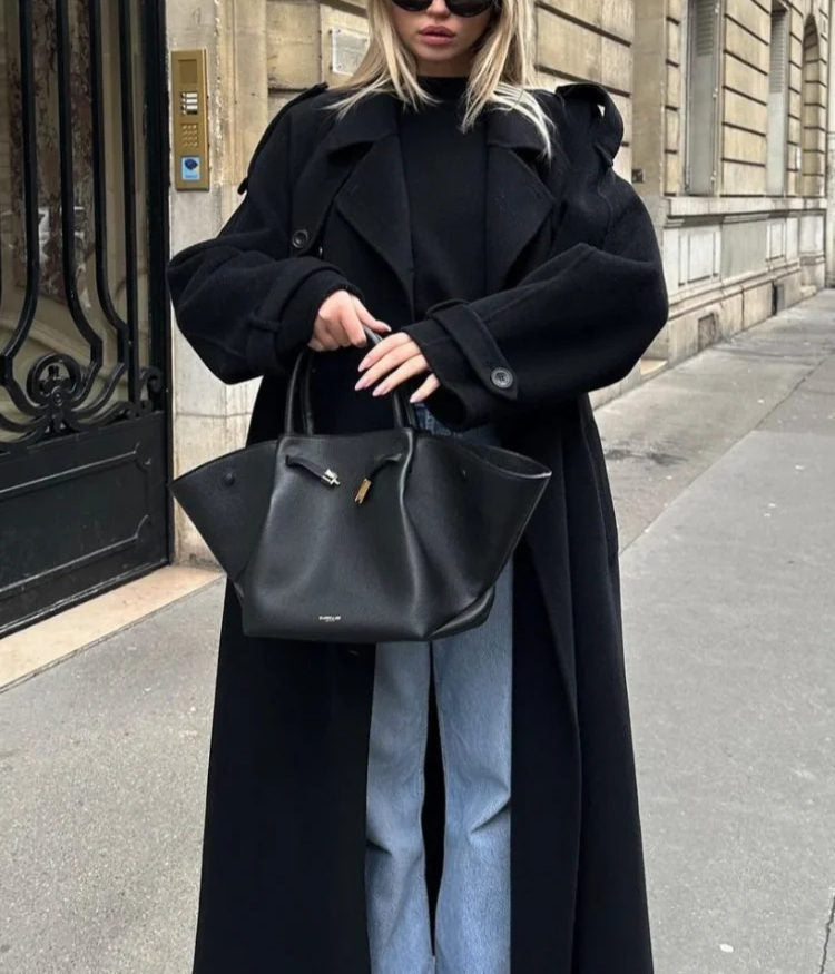 Woman wearing a black longline double-breasted trench coat with wide lapels and a waist belt
