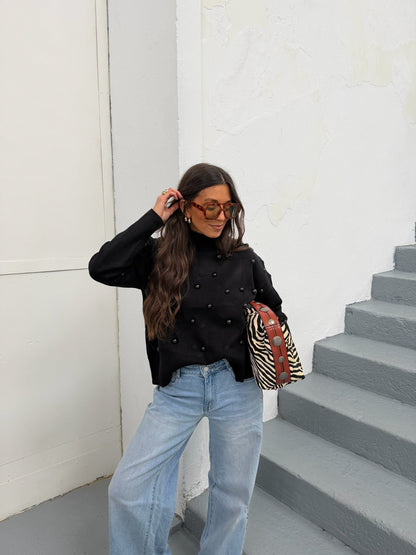 Woman wearing a black mock neck sweater with dark bead embellishments and jeans