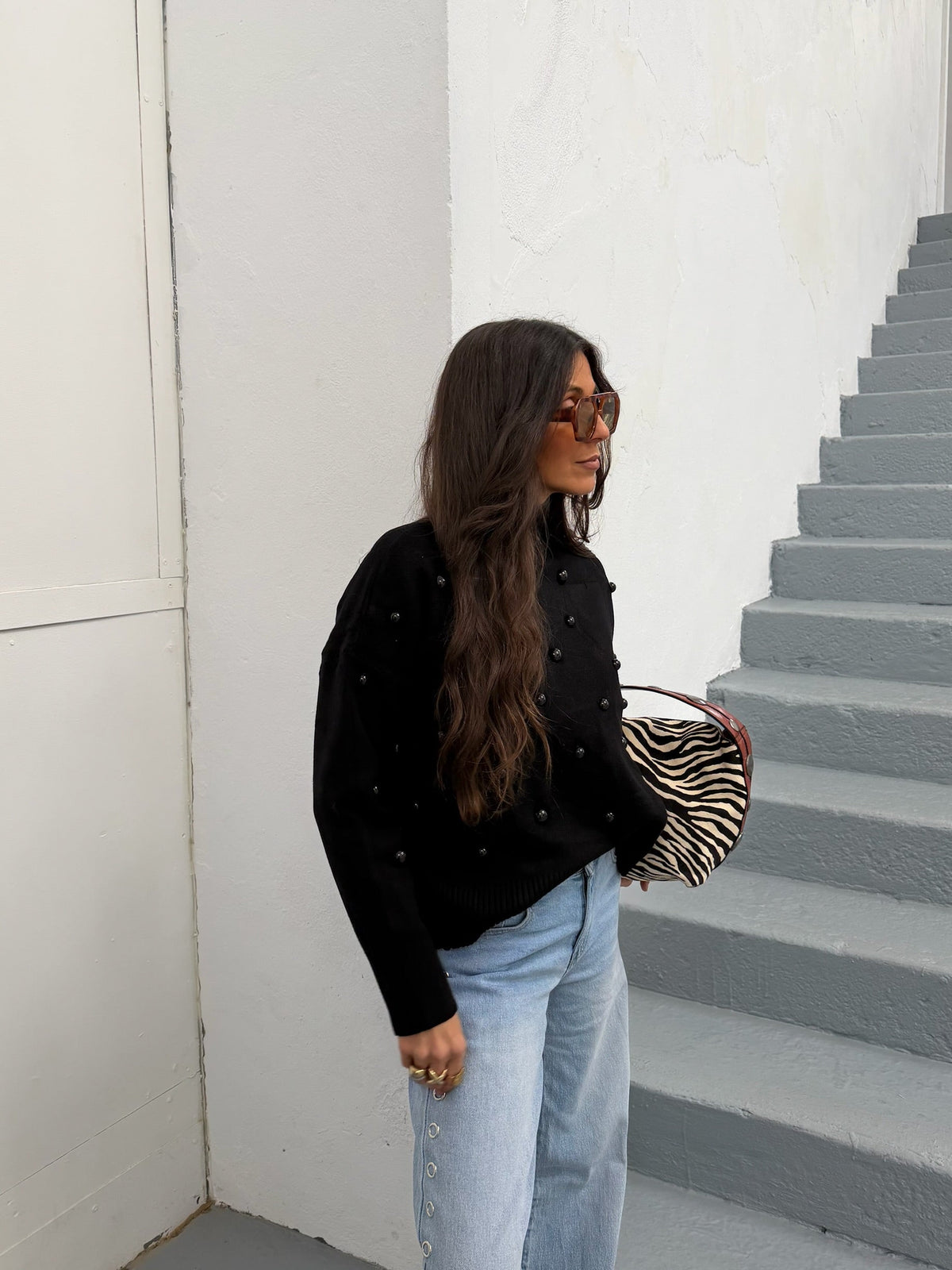 Woman wearing a black mock neck sweater with dark bead embellishments and jeans
