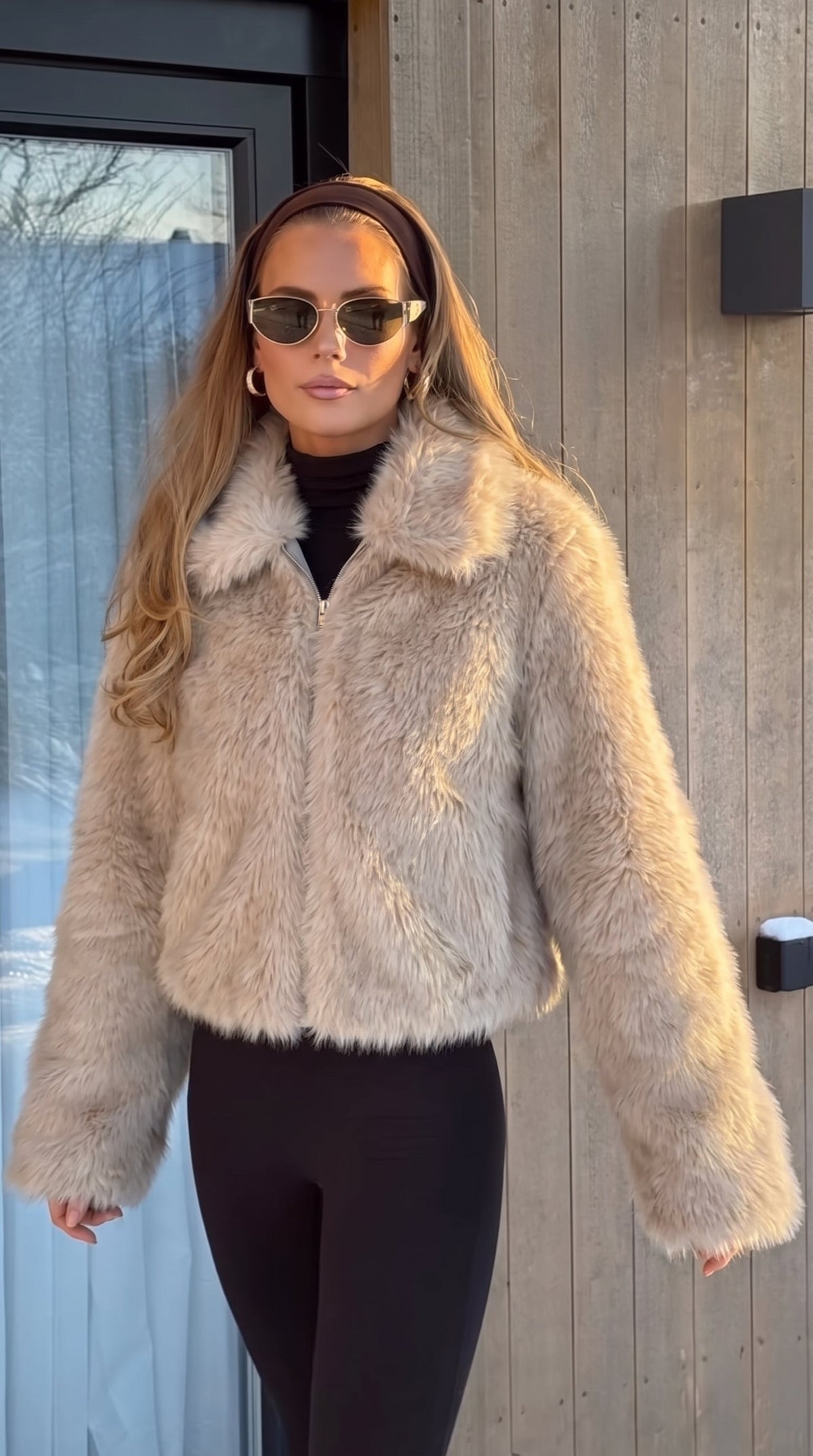 Woman wearing a beige faux fur bomber jacket with a wide collar and long sleeves