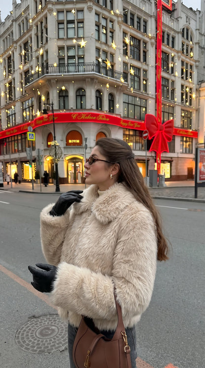 Woman wearing a beige faux fur bomber jacket with a wide collar and long sleeves
