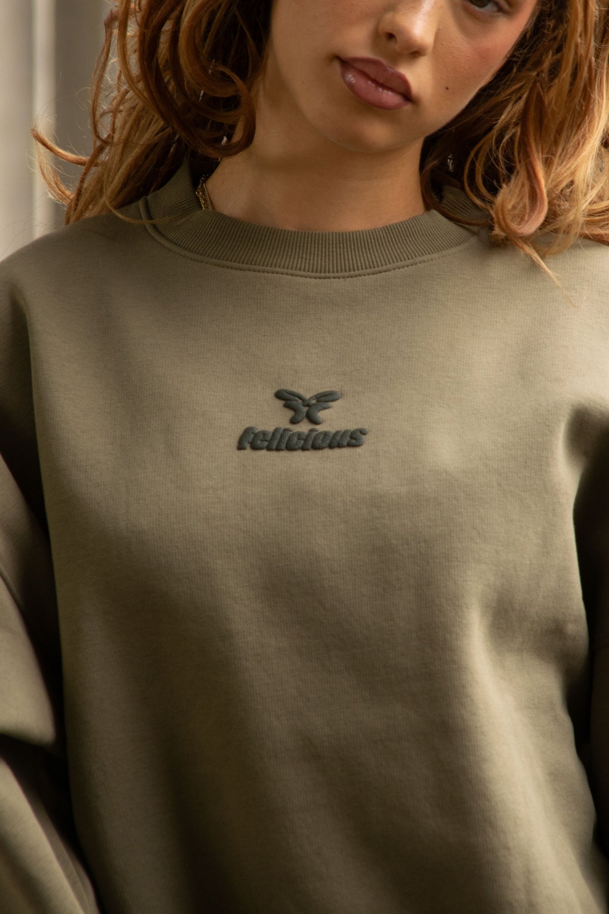 Women's green crewneck sweatshirt with raised chest logo and ribbed trims