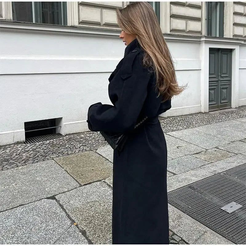 Woman wearing a black longline double-breasted trench coat with wide lapels and a waist belt