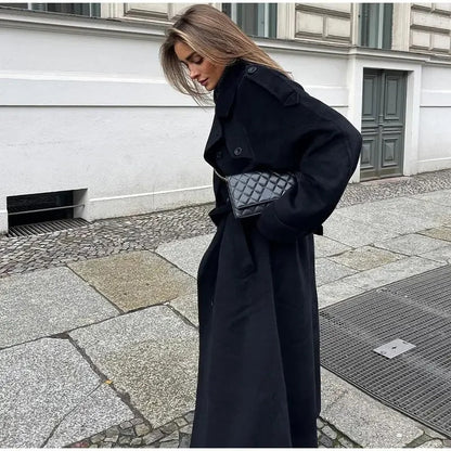 Woman wearing a black longline double-breasted trench coat with wide lapels and a waist belt