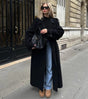 Woman wearing a black longline double-breasted trench coat with wide lapels and a waist belt