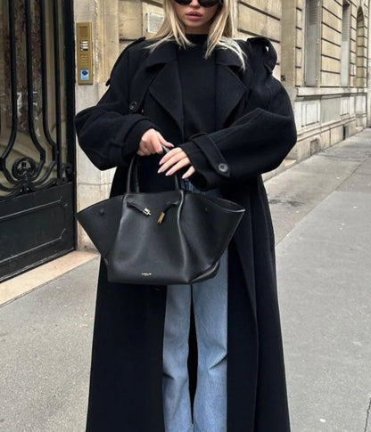 Woman wearing a black longline double-breasted trench coat with wide lapels and a waist belt